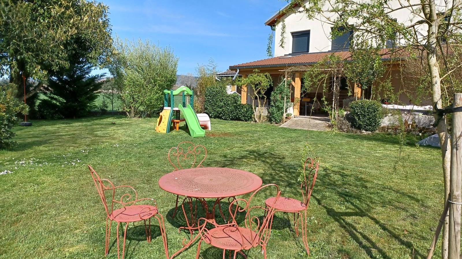 Le jardin clos : pelouse, portique avec toboggan, salon de jardin et la maison d'accueil
